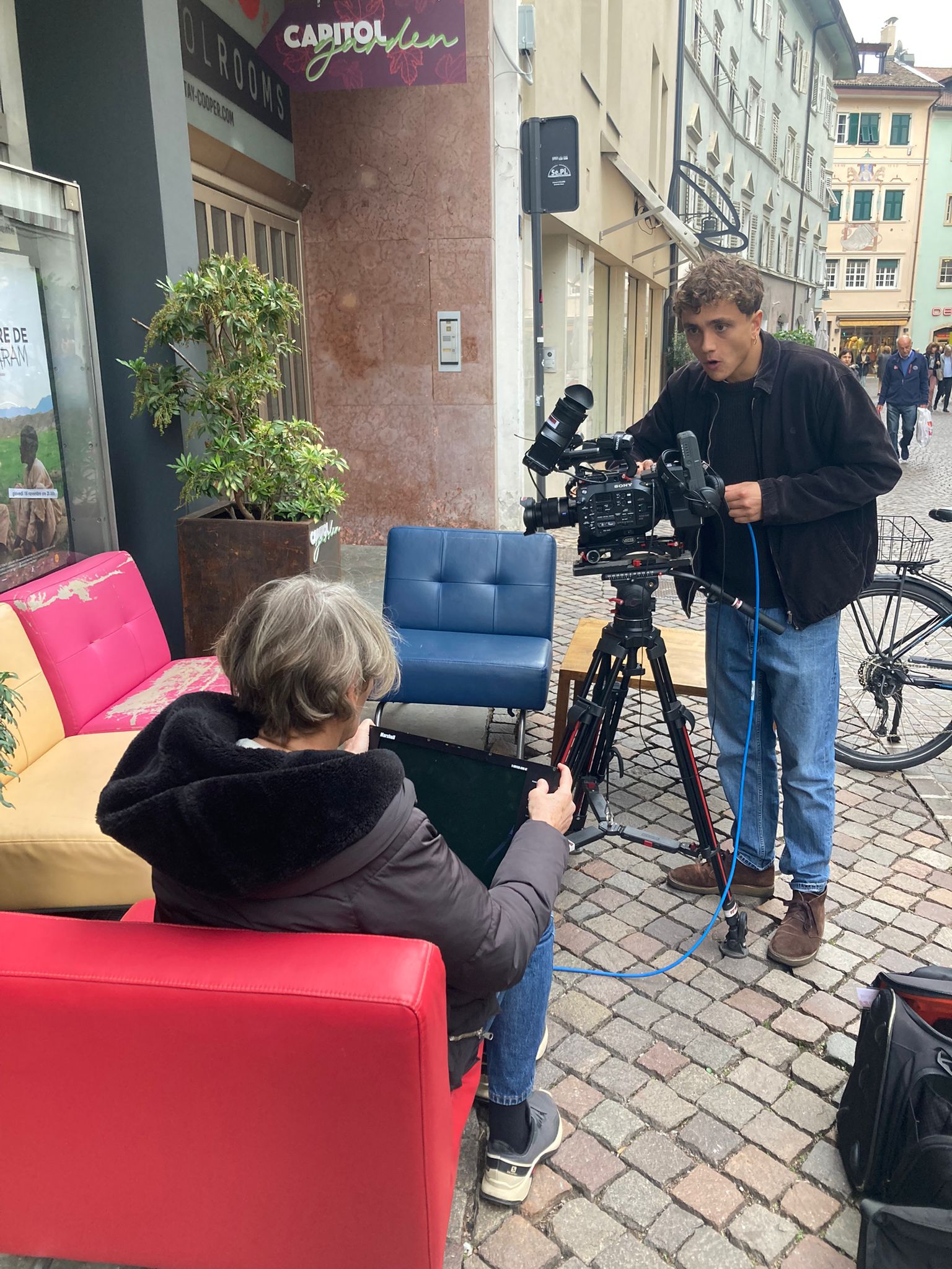 Dietro le quinte di una ripresa video nel centro di Bolzano, con set allestito in strada e cameraman al lavoro.